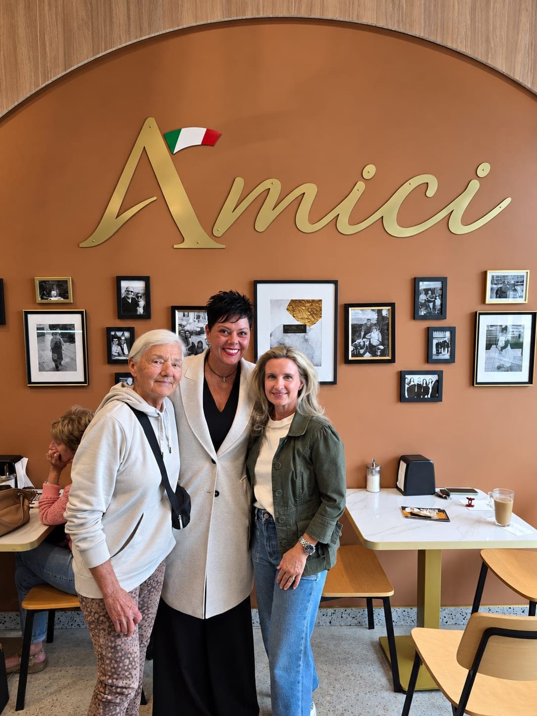 Ivana White with two residents beside a table at Amici Deli & Bakery.